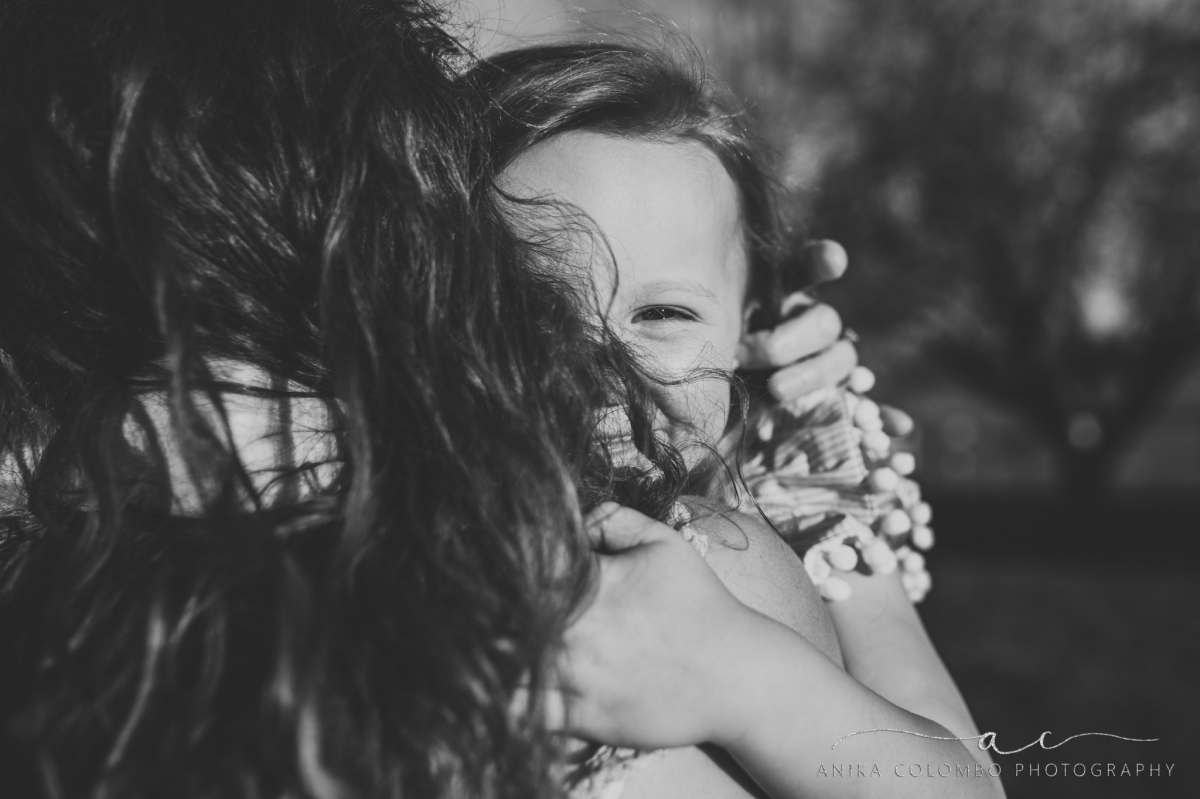 daughter hugging mother's neck and smiling at the camera through her hair
