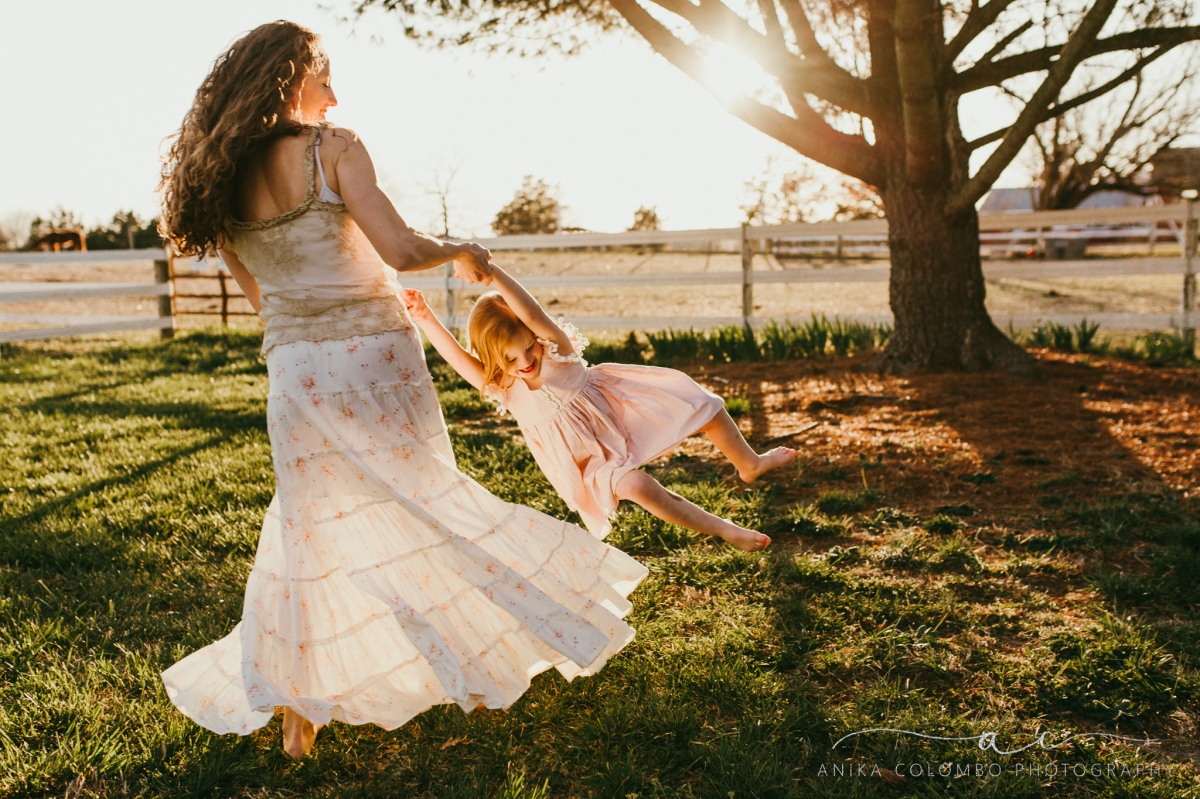 mother swings daughter around with flowing skirts in a field at sunset