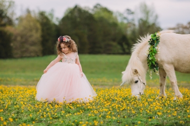little girl in a ballgown with a unicorn in a field of flowers